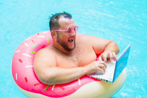 Laughing Fat Funny Man In Pink Inflatable Circle In Pink Glasses Works On A  Laptop In A Swimming Pool Stock Photo - Download Image Now - iStock