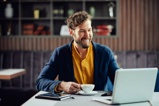 ビジネスマンはコーヒーを飲み、カフェに座りながらノートパソコンを見ている。 - business blue business person businessman ストックフォトと画像