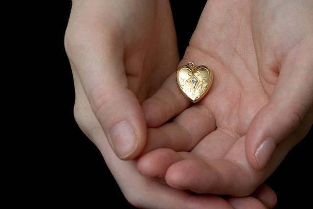 Heart in Hand Color A vintage locket of a heart is held cradled in the palms of a woman's hands, as if she is tentatively offering her heart to someone.  Image is in color. locket stock pictures, royalty-free photos & images