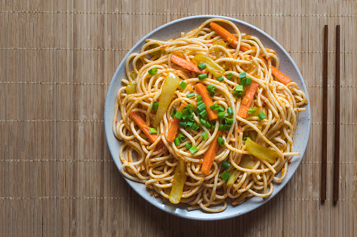 Udon stir fry noodles with chicken and vegetables in a white plate on white background. Top view.