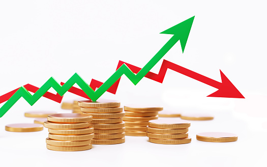 Red and green arrow symbols forming a line graph above coin stacks on white background. High angle view. Horizontal composition with copy space.