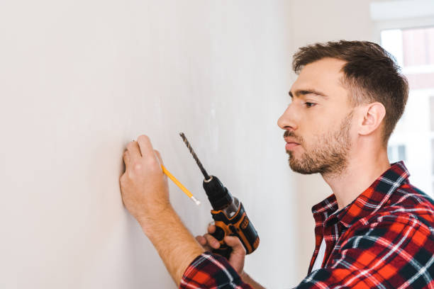 istock handsome man holding drilling machine and pencil in hands while standing near wall 1158882203