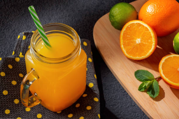 istock Freshly made citrus juice from oranges, grapefruit and lime in a jar-mug with a straw on black table 1158883541