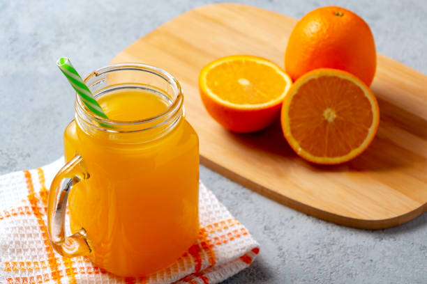 istock Freshly made citrus juice from oranges in a jar-mug with a straw on gray table 1158883571