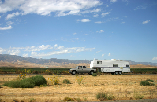 White campervan moving amidst grass on sandy beach against clear blue sky in summer