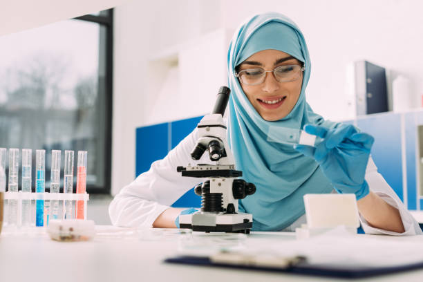 istock smiling female muslim scientist sitting at table with microscope and looking at glass sample during experiment in chemical laboratory 1158885906