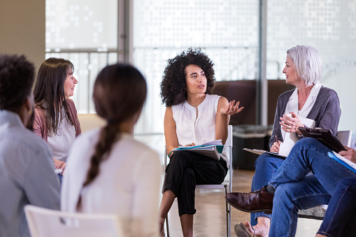 During the weekly group therapy session, a mid adult woman gestures to help explain her problem to the other members.