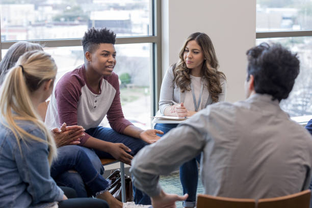 In therapy, teen boy shares life experiences with group As the therapy group members listen, the teen boy shares his life experiences. group therapy photos stock pictures, royalty-free photos & images