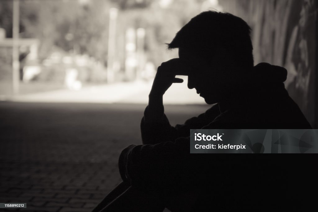 Need a help! Young emotional man in need of help sitting in a sad dark street setting Drug Abuse Stock Photo