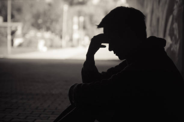 Need a help! Young emotional man in need of help sitting in a sad dark street setting substance abuse stock pictures, royalty-free photos & images