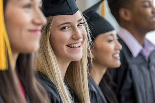 Teen girl smiles at parents before graduation Standing with her fellow graduates, a teen girl smiles with joy at her parents. ceremony photos stock pictures, royalty-free photos & images