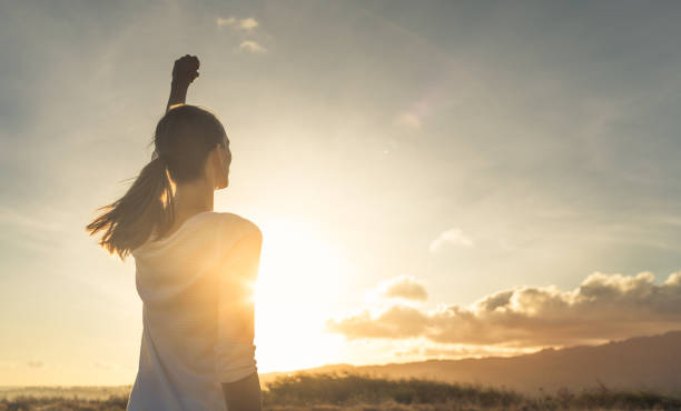 Strong, confident woman with her fist up in the air. Strong, determined, confident woman with her fist up in the air facing sunset. girl power stock pictures, royalty-free photos & images