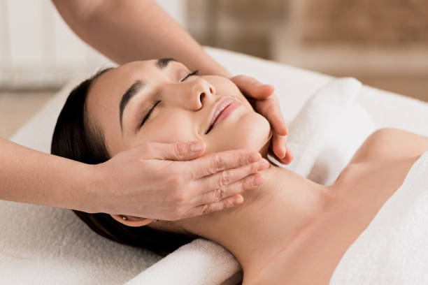 woman getting face massage with closed eyes at spa stock photo