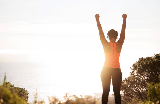 It was worth the climb Rear view of young active woman in sportswear with raised up hands enjoying beautiful sunshine while taking break after workout outside health motivation stock pictures, royalty-free photos & images