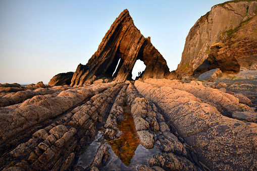 Blackchurch Rock on the North Devon coast glows red at sunset. Near Bideford, distant silhouettes give scale.