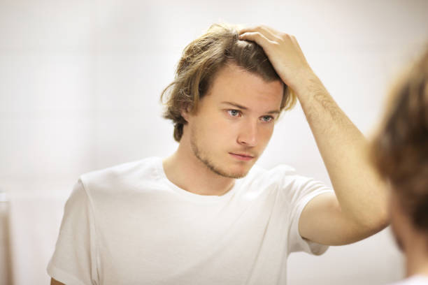 istock young man looking in the mirror,combing his hair,looking at problems on face 1158902471