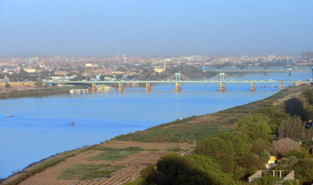 Khartoum downtown agricultural fields and Khartoum North skyline - Blue Nile waterfront - El Mek Nimir bridge, Blue Nile bridge and Armed Forces bridge, Kratoum, Sudan Khartoum, Sudan: Bridges to Khartoum North / Khartoum Bahri: El Mek Nimir bridge, Blue Nile bridge and Armed Forces bridge - View along Nile Street, with agricultural fields on the river bank. khartoum stock pictures, royalty-free photos & images