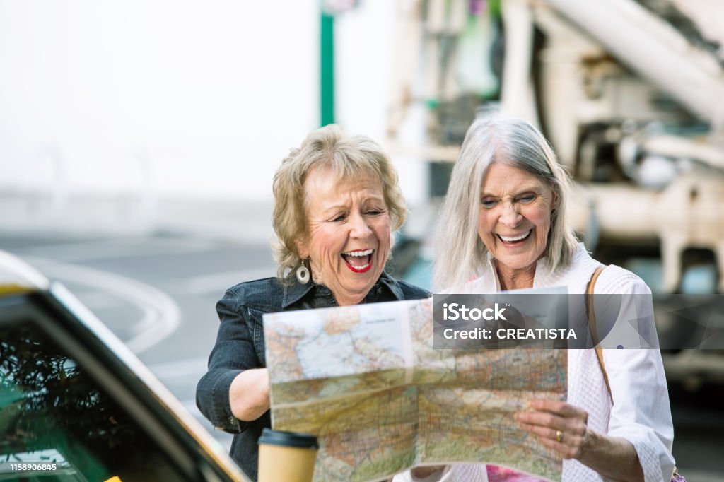 Two Women Checking a Map and Laughing Two laughing women in a city center checking road map Senior Adult Stock Photo