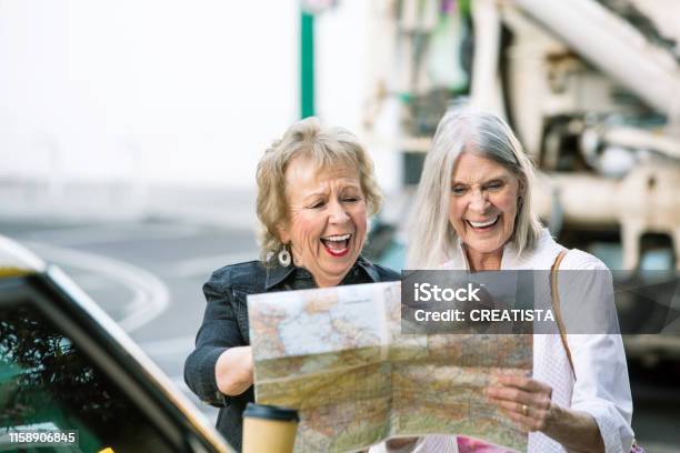 Two Women Checking A Map And Laughing Stock Photo - Download Image Now - Senior Adult, Road Trip, Map