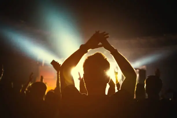 Photo of The bright spotlight shines on the dancing people. The audience applauds the musicians. Silhouette of a concert crowd.