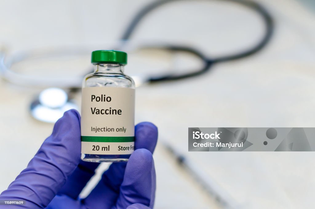 Polio vaccine vial holding in doctors hand Poliomyelitis virus vaccine with stethoscope and syringe at the background Polio Vaccine Stock Photo