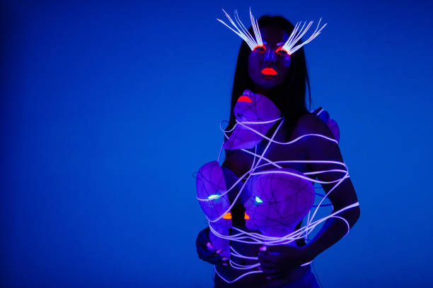 One woman painted with fluorescent make up holding abstract masks. stock photo
