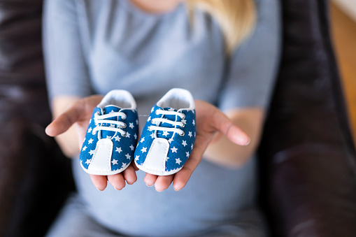 Pregnant woman holding blue baby shoes, focus on foreground.