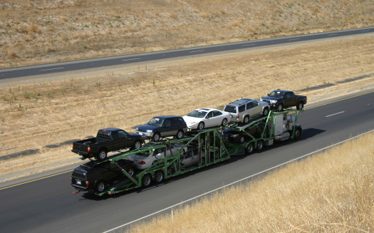 A large truck delivers new cars via highway.