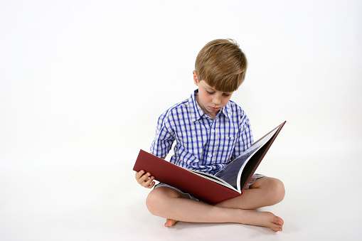Young boy reading a big red cover picture book.     