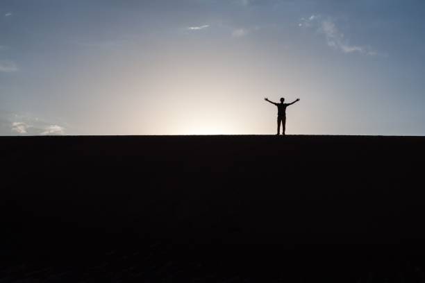istock Raised hand silhouette on a dune in desert. 1158936625