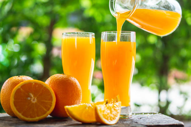 woman hand pouring orange juice on glasses with slice orange on wooden background woman hand pouring orange juice on glasses with slice orange on wooden background, healthy and diet fruit orange juice stock pictures, royalty-free photos & images