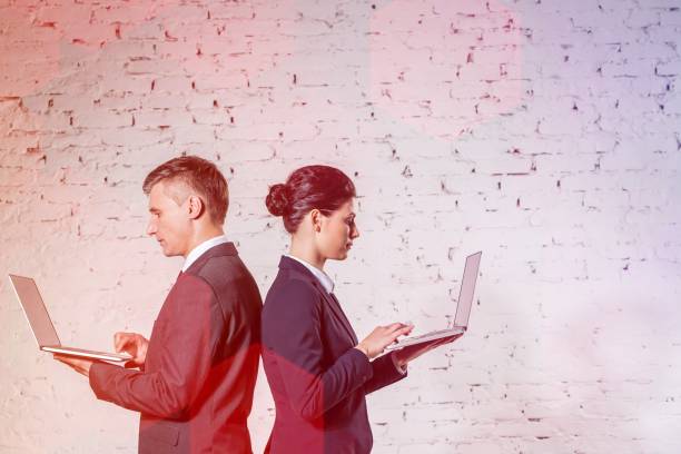 istock Side view of business colleagues using laptops by white brick wall at office 1158981071