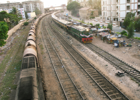 Stationed Oil container on rail tracks while another passenger train is passing by and shanty shakes along the track in midst of high rise apartment buildings. Fact: Cant Station, Karachi, Pakistan.