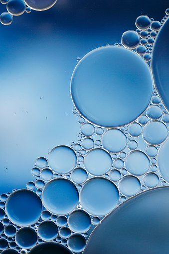 Macro of oil and water bubbles creating a scientific effect image of cell and cell membrane with a blue and white gradient and in a vertical format.