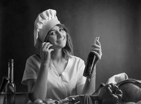 Young woman in a chef uniform with small bottles of olive oil. Fragrant olive oil with various spices and herbs. Black and white.