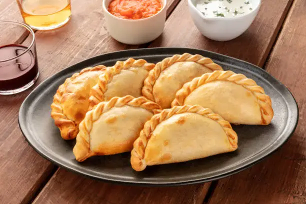 Photo of A closeup of Argentinian empanadas with sauces and wine on a dark rustic wooden background