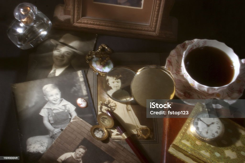 Memories collection. Antique, vintage photographs, collectibles. Collection of vintage photographs, one highlighted through a magnifying glass.  Cup of coffee, old pocket watch, locket, necklace, choaker locket, perfume bottle,  cameo and fountain pen.  Diffused, soft lighting creates the scene and atmosphere. Retro, old-fashioned.  Photograph Stock Photo