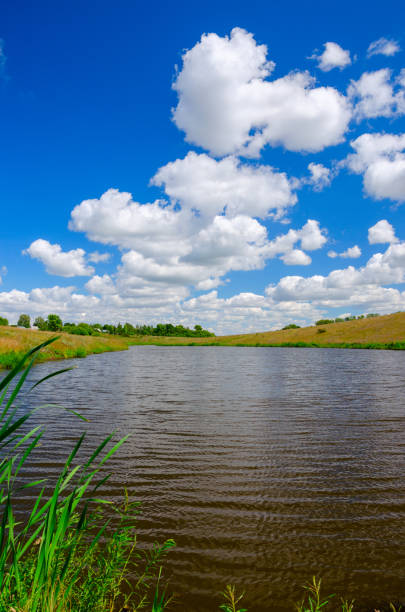 istock Sunny summer landscape with river,fields,green hills and beautiful clouds in blue sky. 1159004252