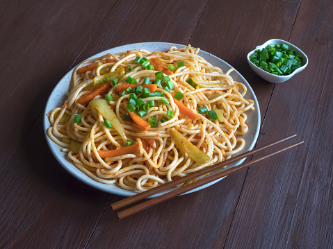 Schezwan Noodles with vegetables in a plate on a dark wooden table.