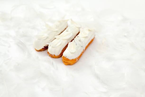 A set of three eclairs with white chocolate decor isolate on a white surface decorated with white feathers