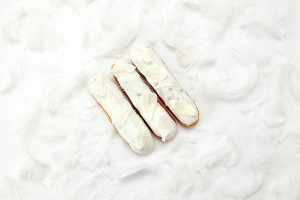 A set of three eclairs with white chocolate decor isolate on a white surface decorated with white feathers