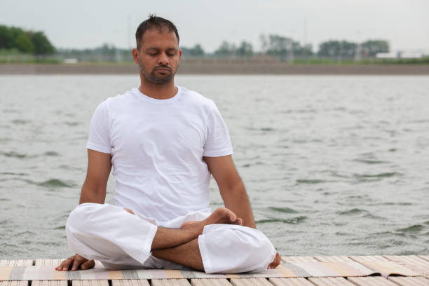 istock Young man doing yoga and meditating in warrior pose on beach 1159005136