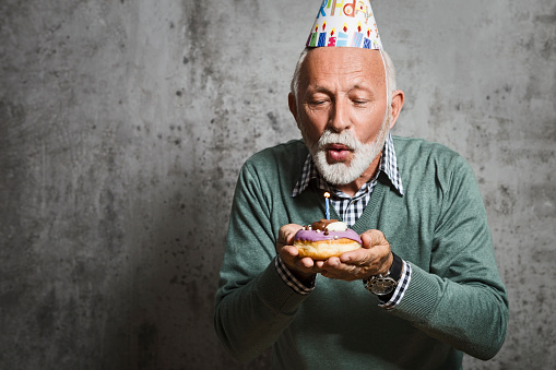 istock Senior man blowing candles with birthday hat 1159007871