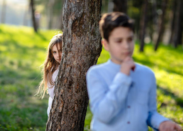 Girl and boy playing hide and seek in park. Jalousie girl watching on boyfriend. Girl hiding from boy in park.