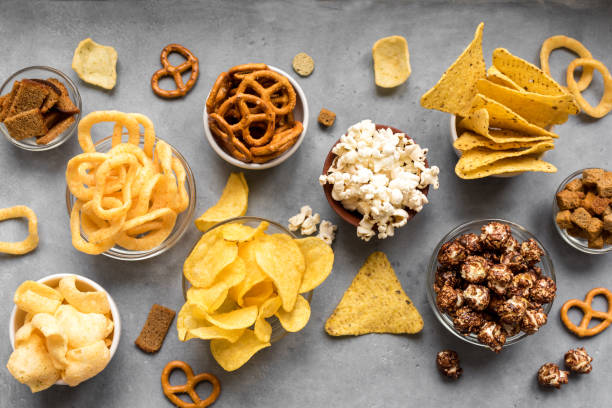Unhealthy Snacks Assortment of Unhealthy Snacks: chips, popcorn, nachos, pretzels, onion rings in bowls, top view, copy space. Unhealthy eating concept. preserved food stock pictures, royalty-free photos & images