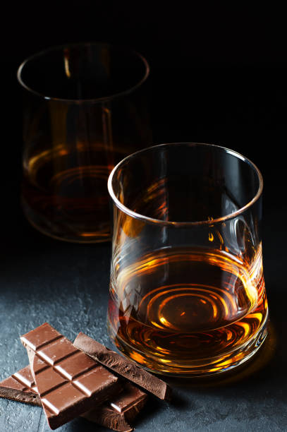 cognac o rum o bourbon in un bicchiere. pezzi di cioccolato. degustazione di alcol. sfondo scuro - brown chocolate candy bar close up foto e immagini stock