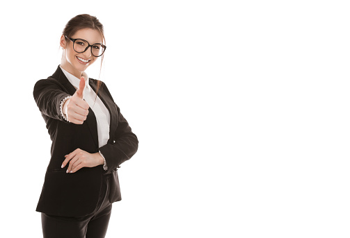 Closeup cutout portrait of a beautiful woman showing thumb up like, approval sign with finger, hand, happy smiling girl wearing formal black suit and white shirt isolated on a pure white background
