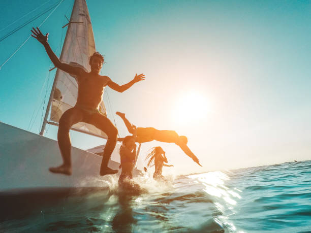 amici pazzi che si tuffano dalla barca a vela in mare - giovani che saltano all'interno dell'oceano durante le vacanze estive - focus principale sull'uomo sinistro - concetto di viaggio e divertimento - acqua sulla macchina fotografica - lake summer beach nautical vessel foto e immagini stock