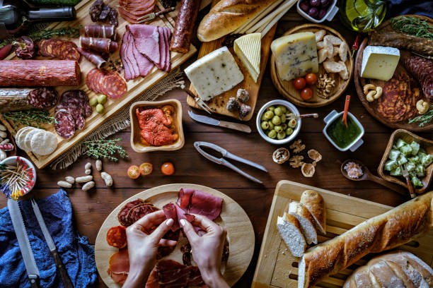 istock Female hands preparing snacks and appetizers in a set full of assorted Cured ham and cheese on rustic wood 1159016530