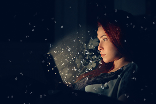 side view of young woman in night time holding digital tablet and reading.